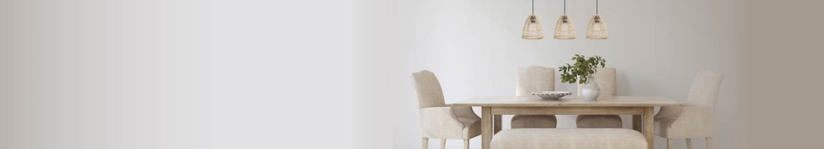 A light wood dining table with six neutral chairs in a bright, minimalist dining room; three woven pendant lights hang above and a small plant sits in the center.