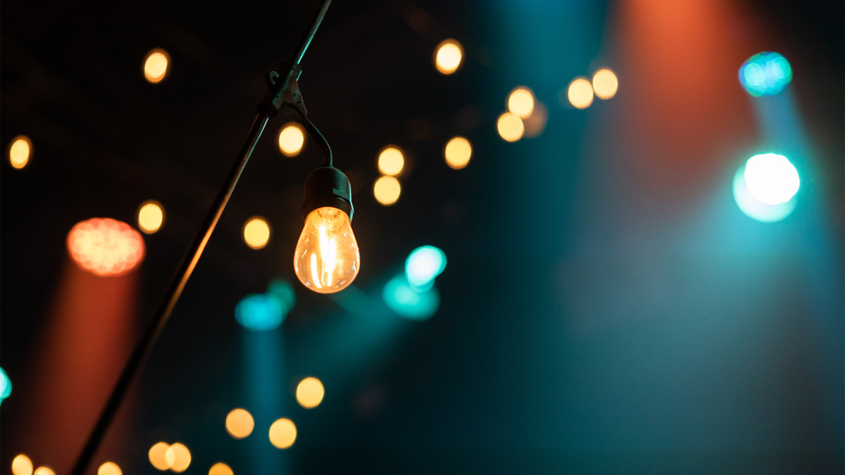 bokeh-lights | Eglo Romania Close-up of an illuminated Edison bulb with colorful string lights in the blurred background, creating a warm, festive atmosphere.